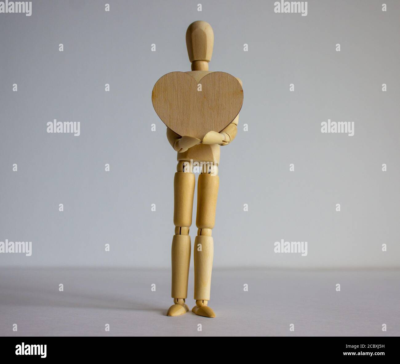 COVID-19 concetto di coronavirus pandemico. Modello di legno di un uomo che tiene un cuore di legno. Spazio vuoto per il testo. Foto Stock