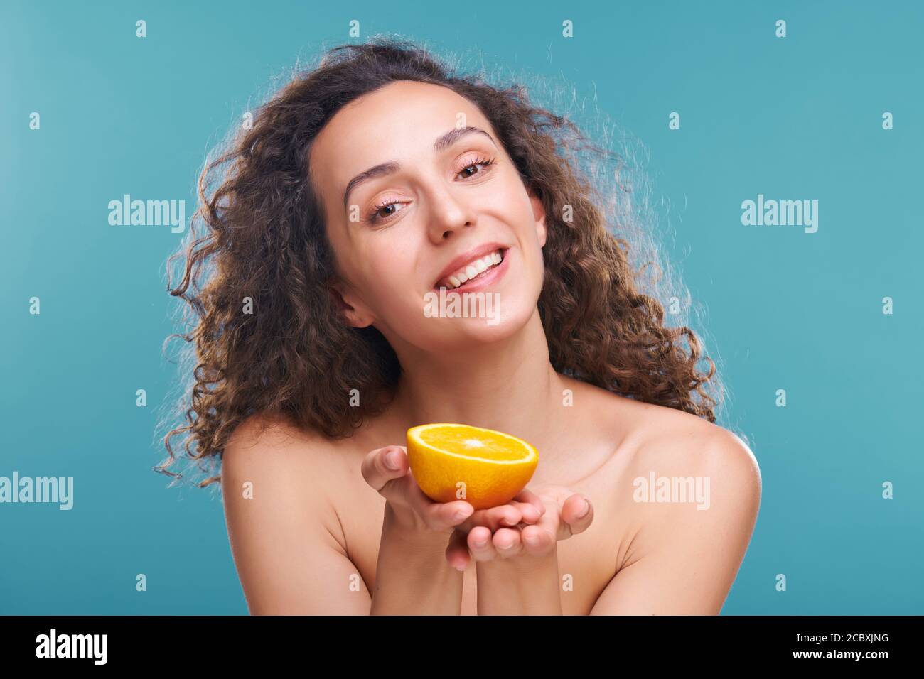 Giovane donna sana con il sorriso toothy che vi offre metà di arancio fresco e succoso Foto Stock