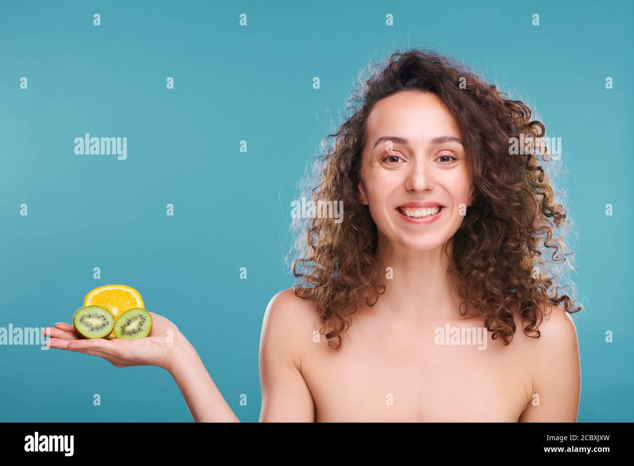 Donna sana con un sorriso toothy che tiene metà di fresco succosa arancio e kiwi Foto Stock