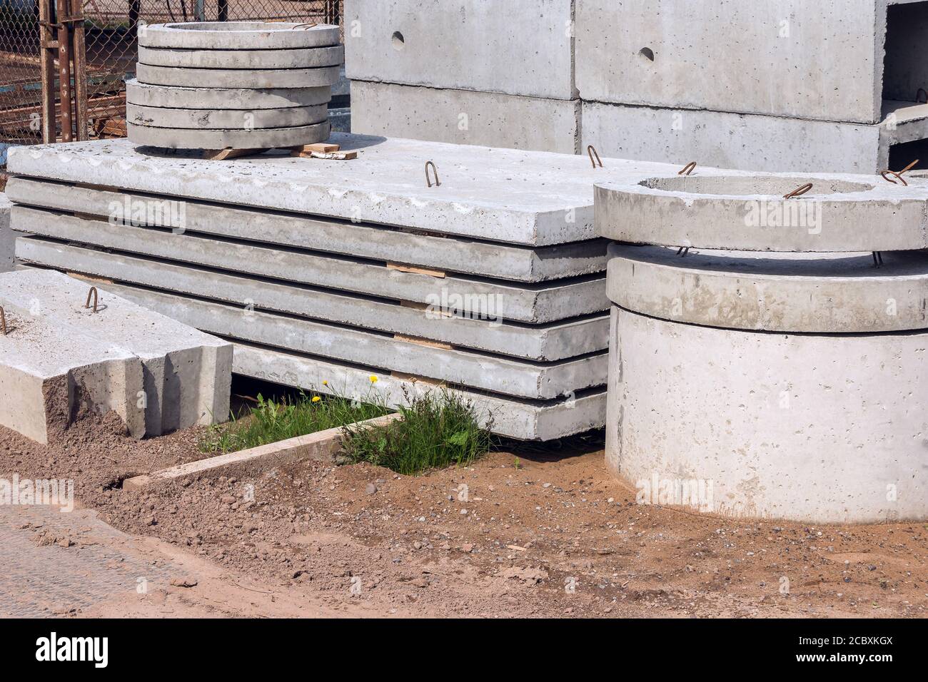Lastre e anelli in cemento armato per l'impianto fognario in cantiere. Produzione industriale di prodotti cementizi. Foto Stock