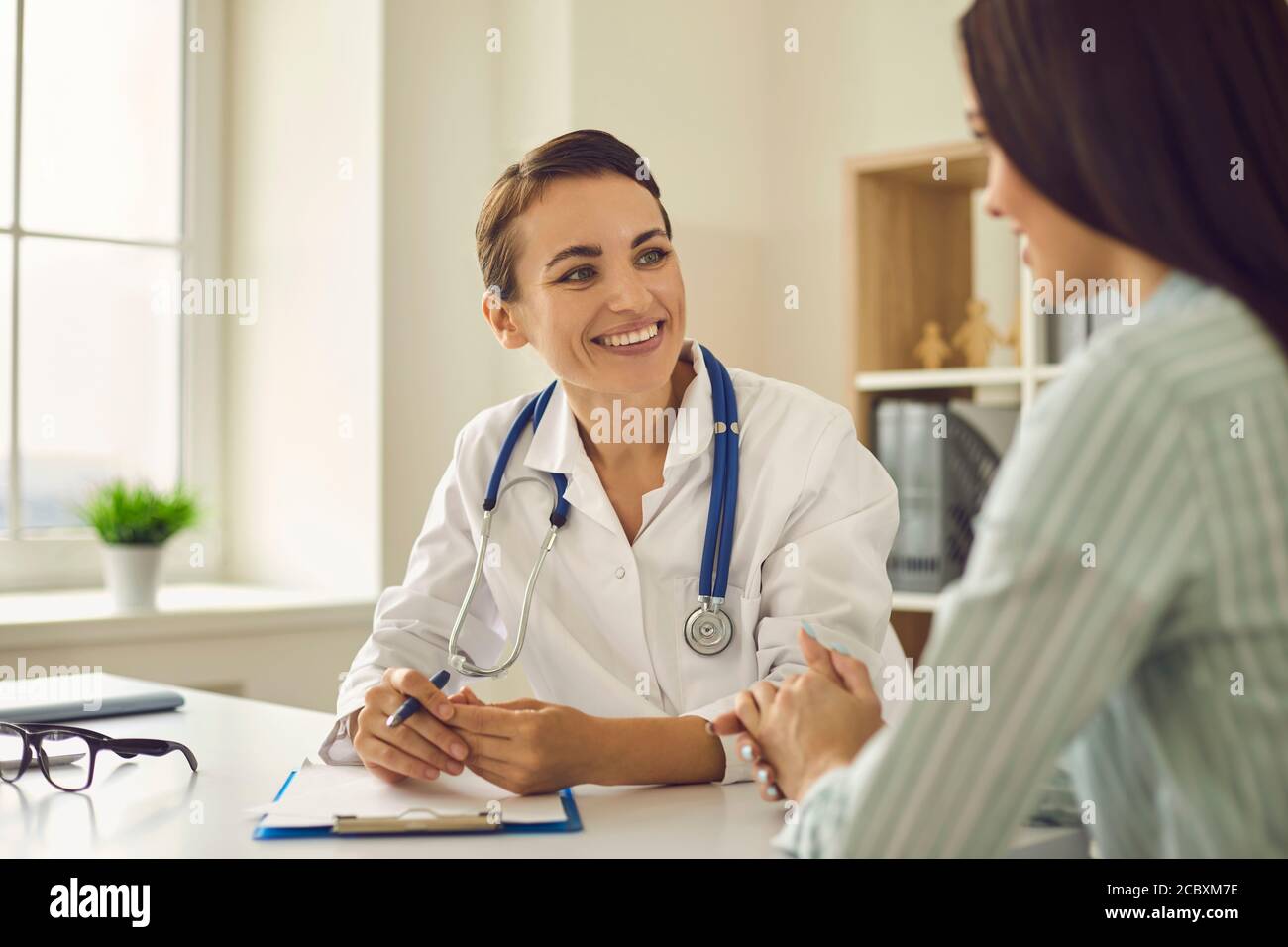 Giovane medico che parla con paziente di donna in clinica durante la visita Foto Stock