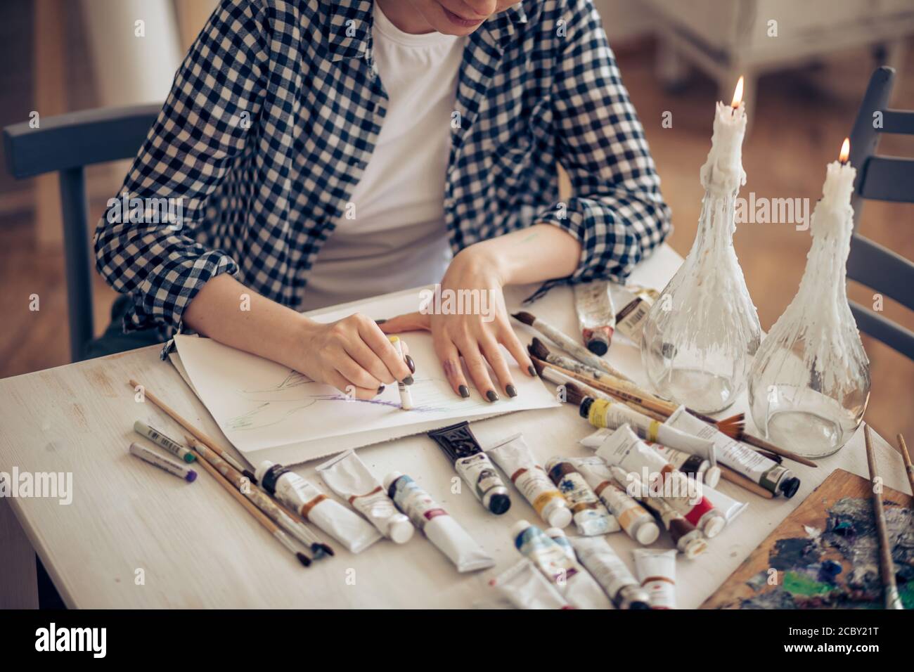 primo piano foto ritagliata. le mani di una giovane donna tengono il pastello e disegnano qualcosa sulla carta sul tavolo con diversi strumenti dell'artista Foto Stock