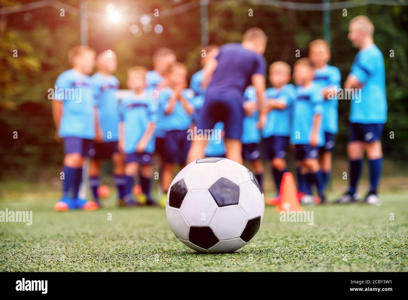 Pallone da calcio e squadra di calcio giovanile offuscata con allenatore il campo Foto Stock
