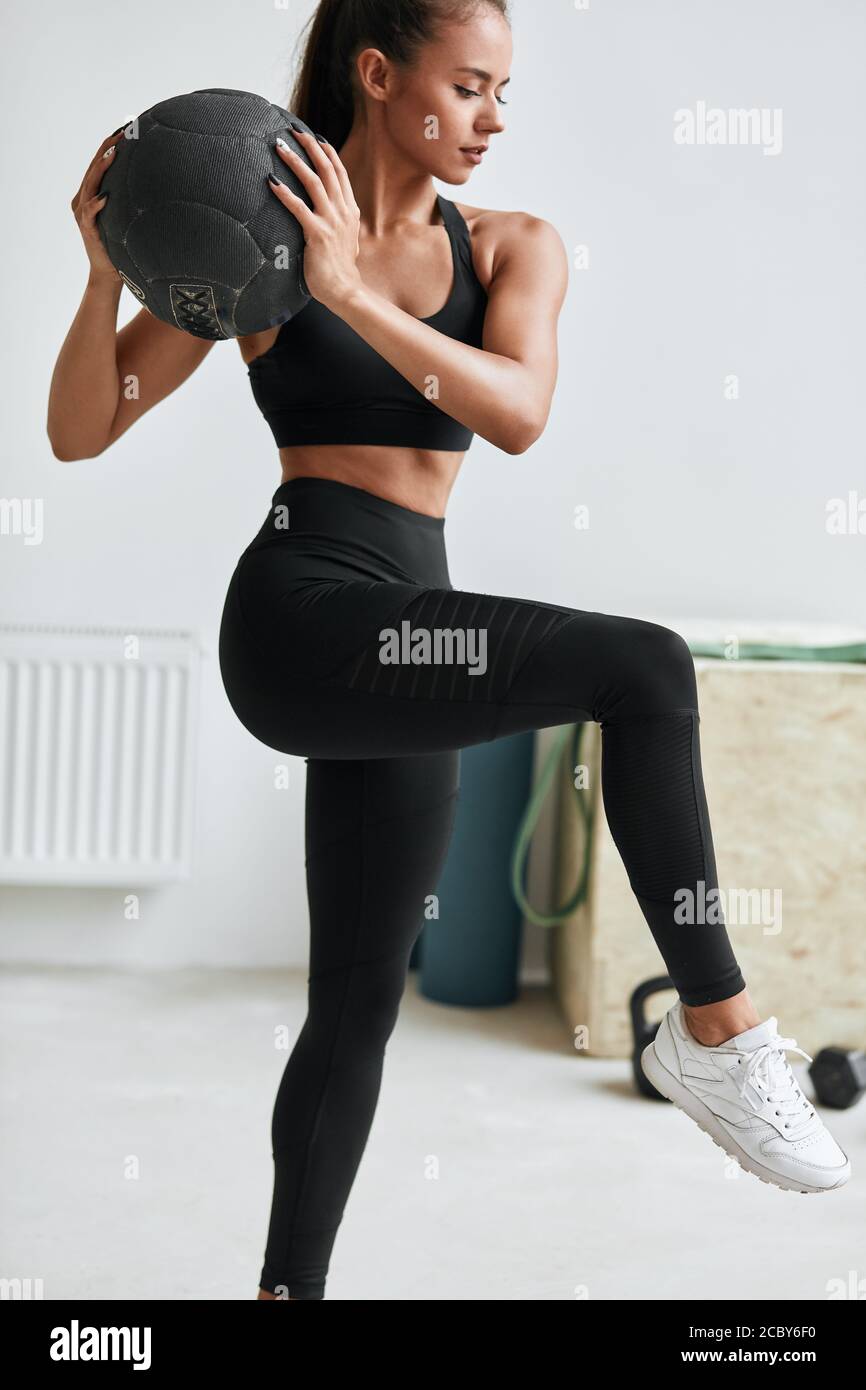 Donna sportiva che allunga le gambe con l'aiuto di palle. Ragazza caucasica in swears nero sportivo. Sfondo bianco Foto Stock