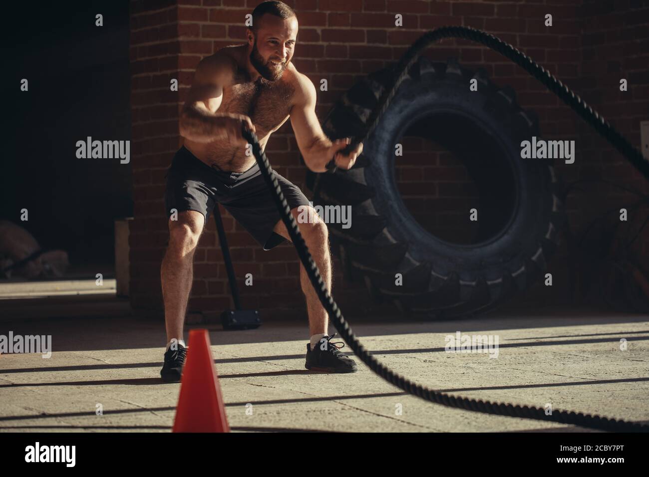 Potente muscolare determinato uomo con formazione di corda in allenamento funzionale in palestra esterna con pareti in mattoni, rafforzare i muscoli delle spalle, w Foto Stock