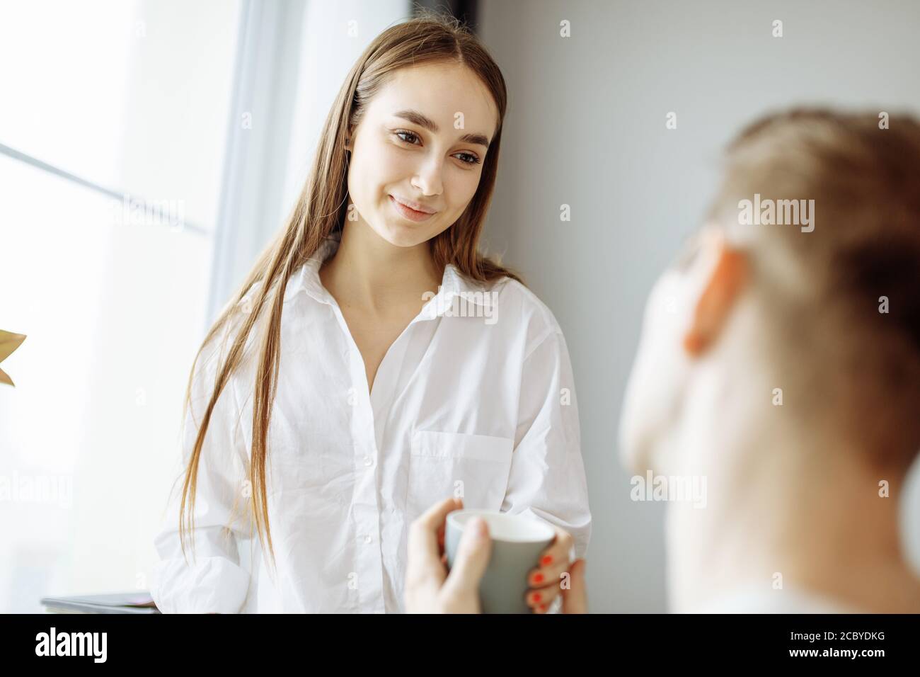 carina signora caucasica parlare bene con il marito al mattino. donna sorridere e guardare l'uomo con amore mentre è seduto sulla sedia. famiglia, relazioni Foto Stock