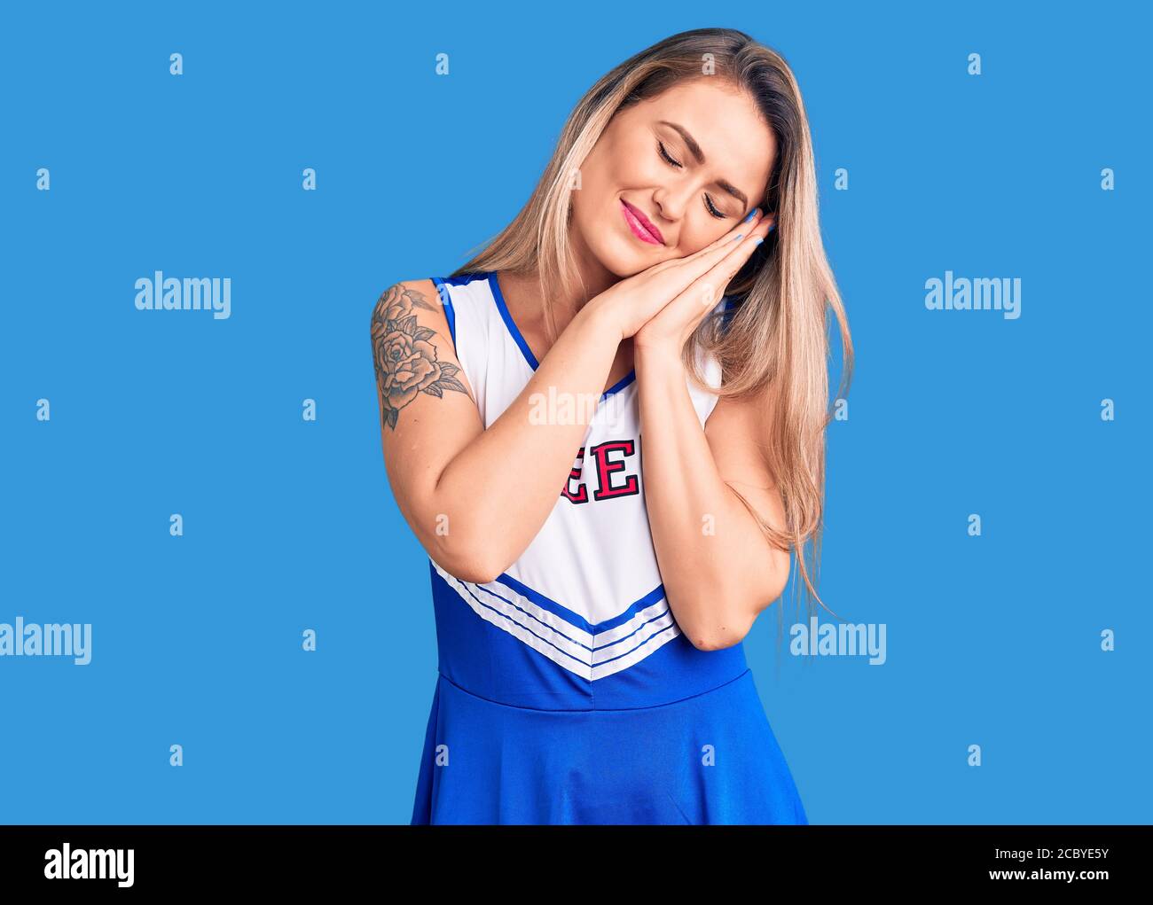 Giovane bella donna bionda che indossa uniforme cheerleader dormire stanco sognare e posare con le mani insieme mentre sorride con gli occhi chiusi. Foto Stock