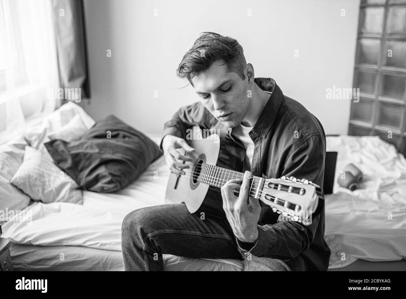 uomo caucasico autodidatta prova a suonare la chitarra acustica a casa, imparare una nuova canzone, suonare la chitarra è hobby, tempo libero a casa. foto in bianco e nero Foto Stock