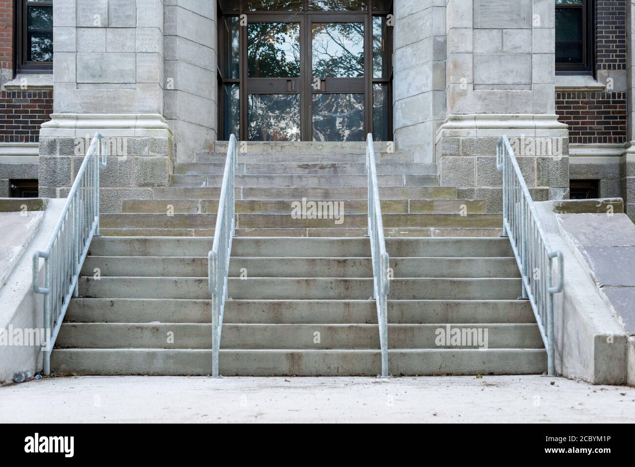 La parte anteriore di un edificio neocolonialista con scalini di granito e ringhiere di ferro grigie. L'edificio ha 2 colonne e un'alta porta di vetro. Foto Stock