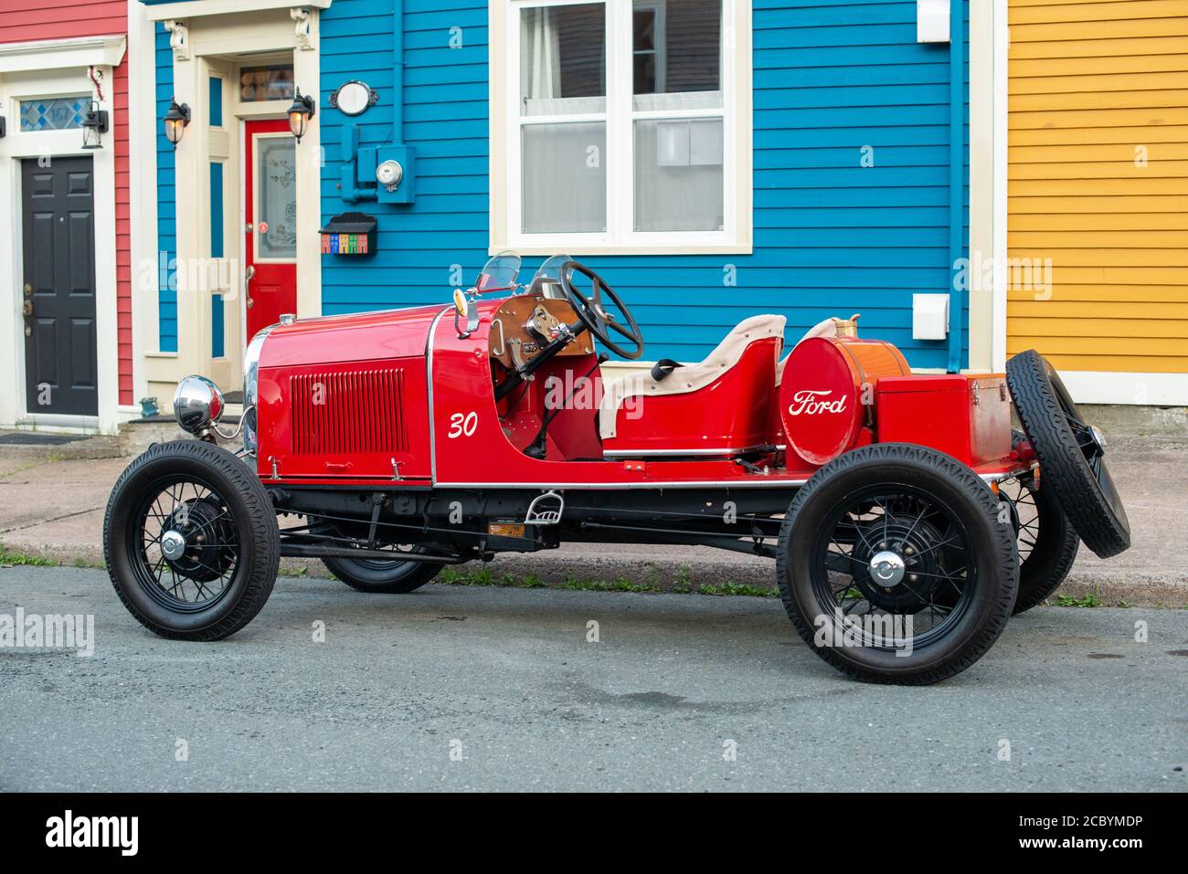 Un modello UN'auto Ford si siede inutilizzato al di fuori di più case colorate di fila nel centro di St. John's. La vettura è di colore rosso brillante con pneumatici neri e interni abbronzati. Foto Stock