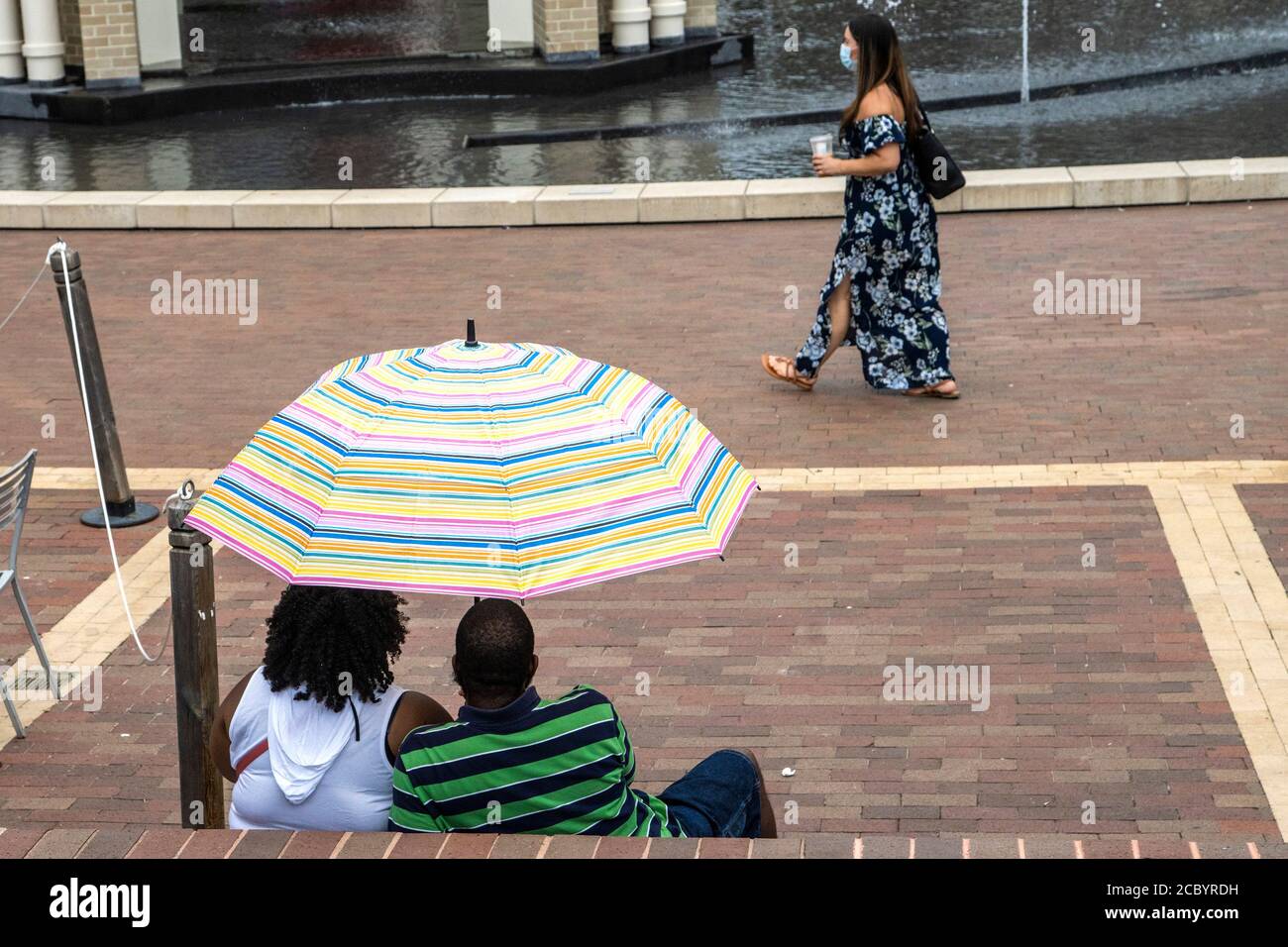 Una coppia riparata sotto un ombrello guarda un passerby. Foto Stock