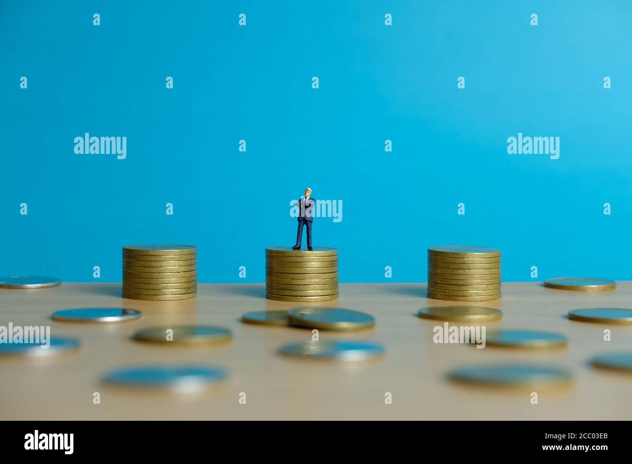 Concetto di business in miniatura - uomo d'affari in piedi sopra la moneta d'oro impilare Foto Stock