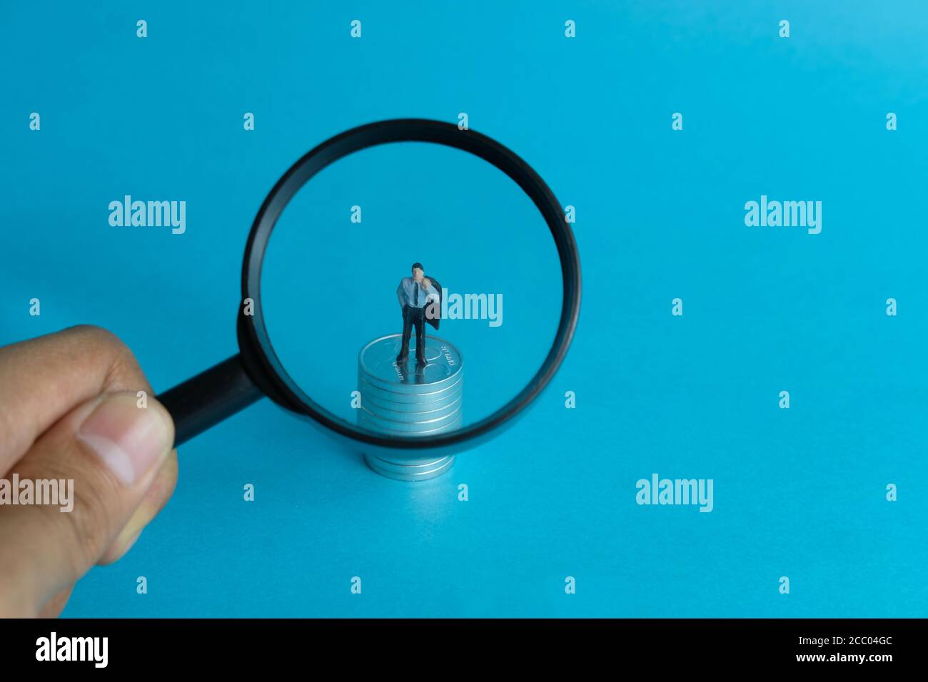 Concetto di affari in miniatura - uomo d'affari depresso di ingrandimento di cui in piedi sopra pila di monete Foto Stock