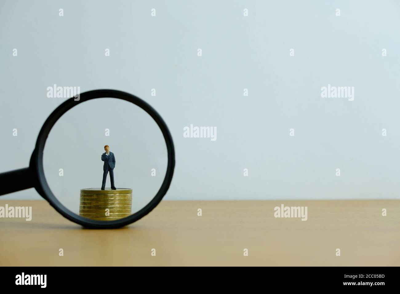 Concetto di business di persone in miniatura - un uomo d'affari in piedi su pila di monete con lente di ingrandimento, alla ricerca di soluzione finanziaria / strategia Foto Stock