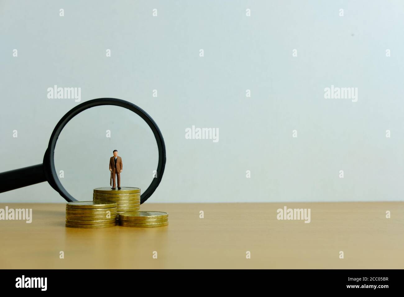 Concetto di business di persone in miniatura - un uomo d'affari in piedi su pila di monete con lente di ingrandimento, alla ricerca di soluzione finanziaria / strategia Foto Stock