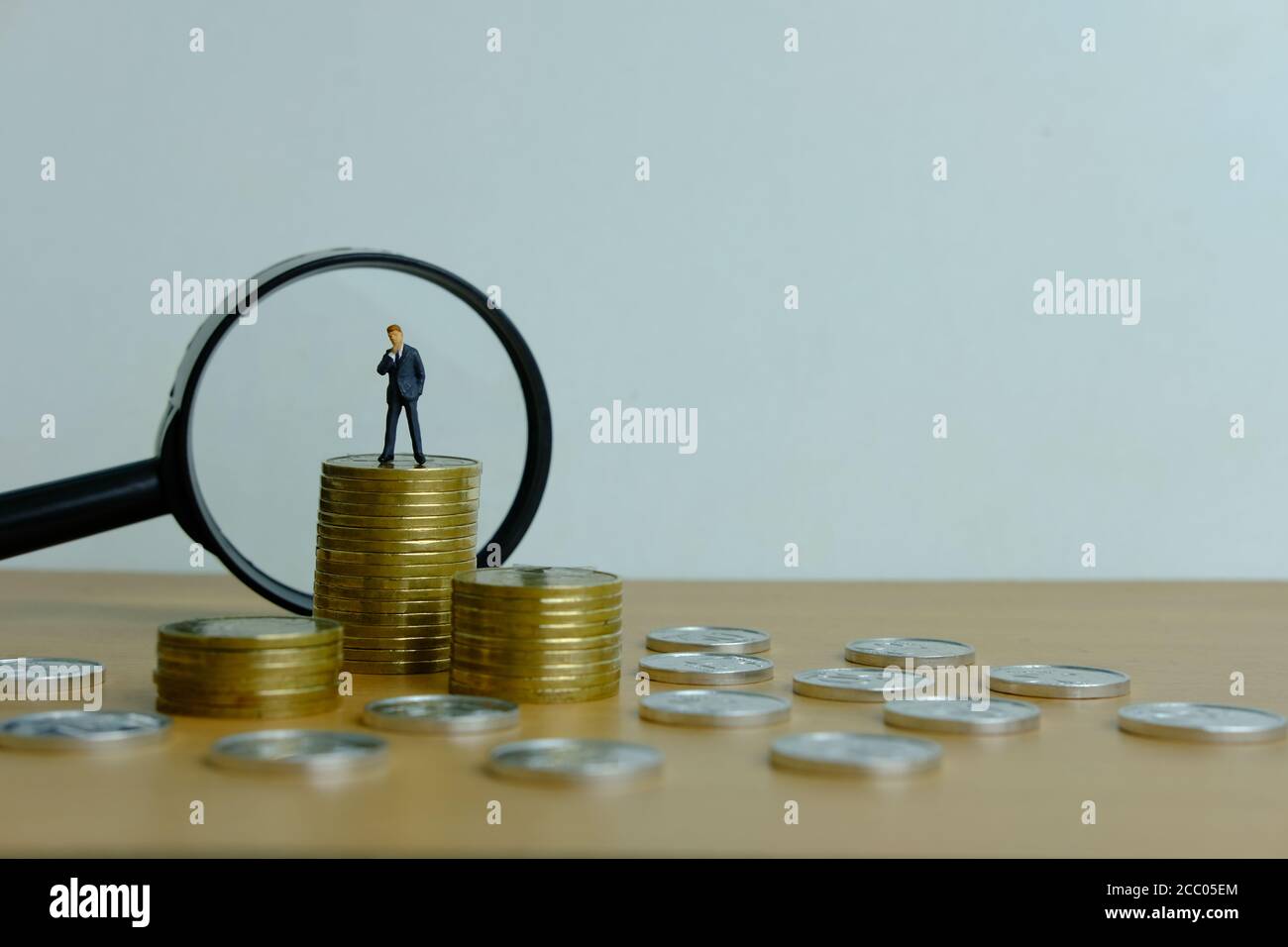 Concetto di business di persone in miniatura - un uomo d'affari in piedi su pila di monete con lente di ingrandimento, alla ricerca di soluzione finanziaria / strategia Foto Stock