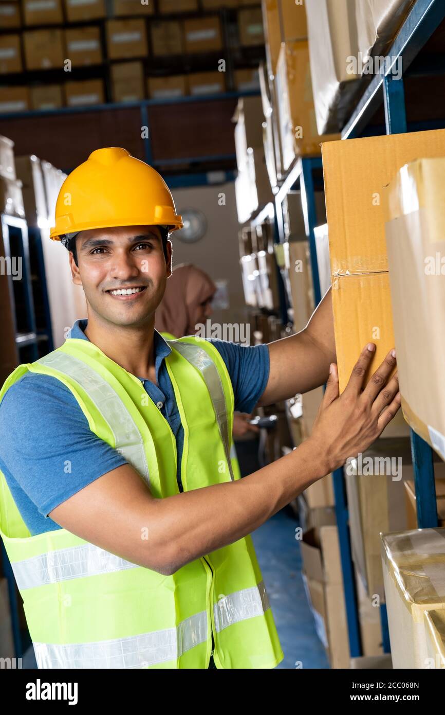 Ritratto del lavoratore indiano di magazzino messo scatola di cartone in scaffale con operaio asiatico musulmano fare l'inventario nel magazzino ambiente di centro di distribuzione. Foto Stock