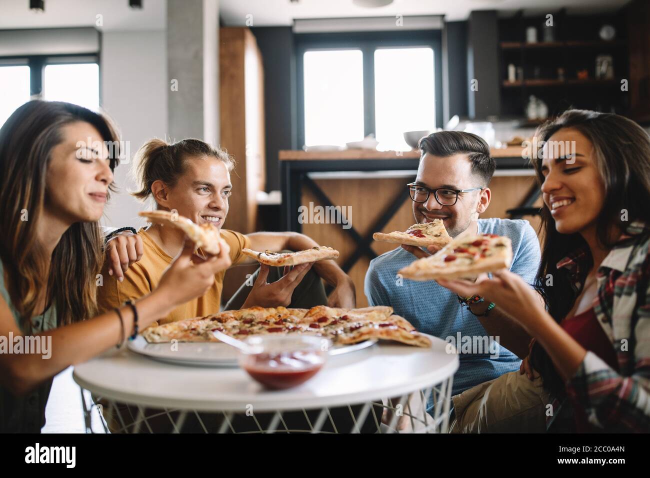 Gruppo allegro di amici che si divertono a casa, mangiare pizza. Foto Stock