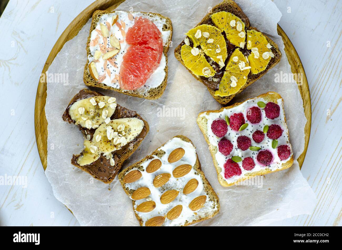 Colazione sana con burro di arachidi, banana, cioccolato, semi di chia, lamponi, mandorla, yogurt, arance, pompelmo. Piastra di legno Foto Stock
