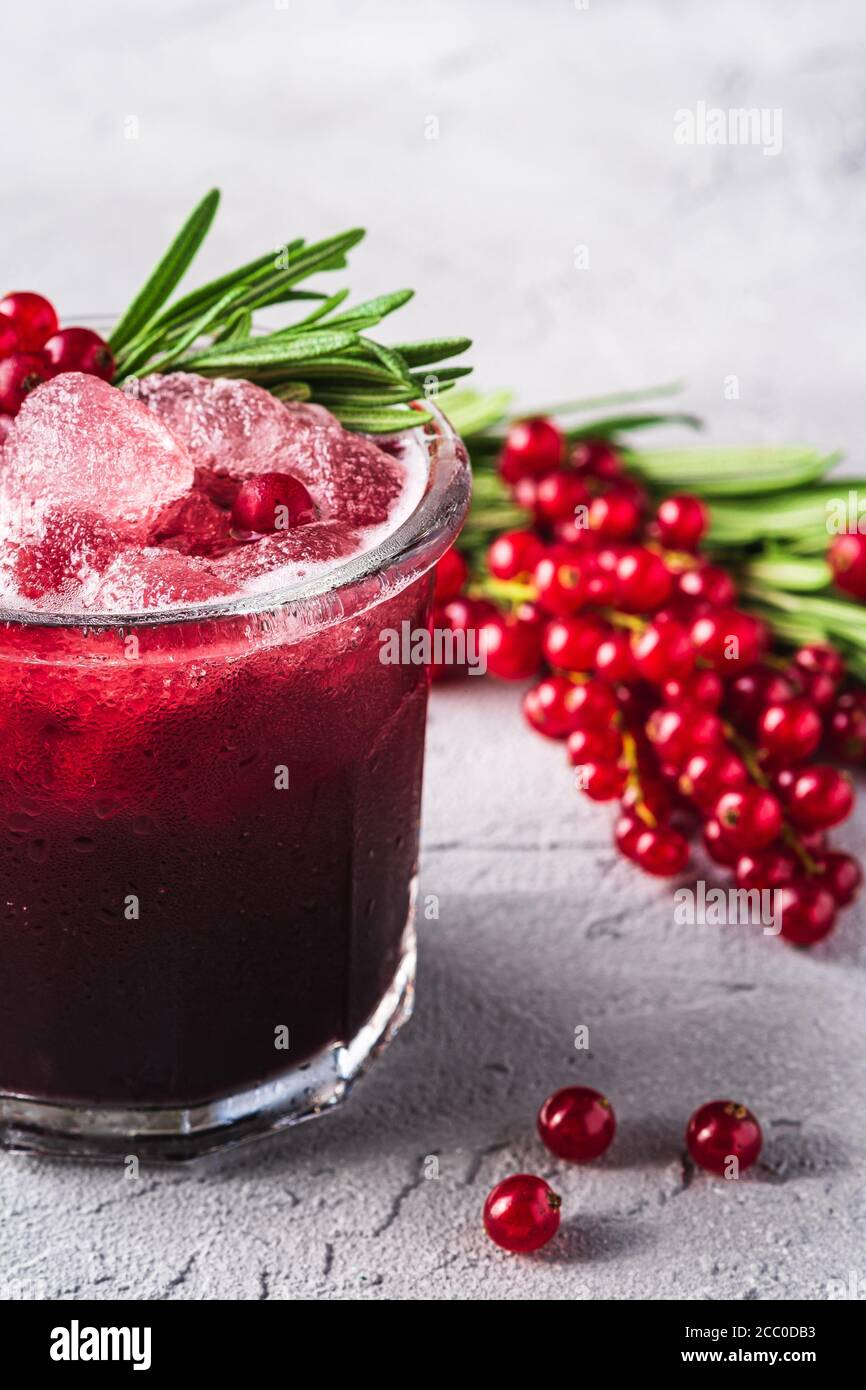 Cocktail di frutta fresca ghiacciata in vetro, rinfrescante bevanda estiva al ribes rosso con foglia di rosmarino su fondo di pietra in cemento, vista angolare Foto Stock