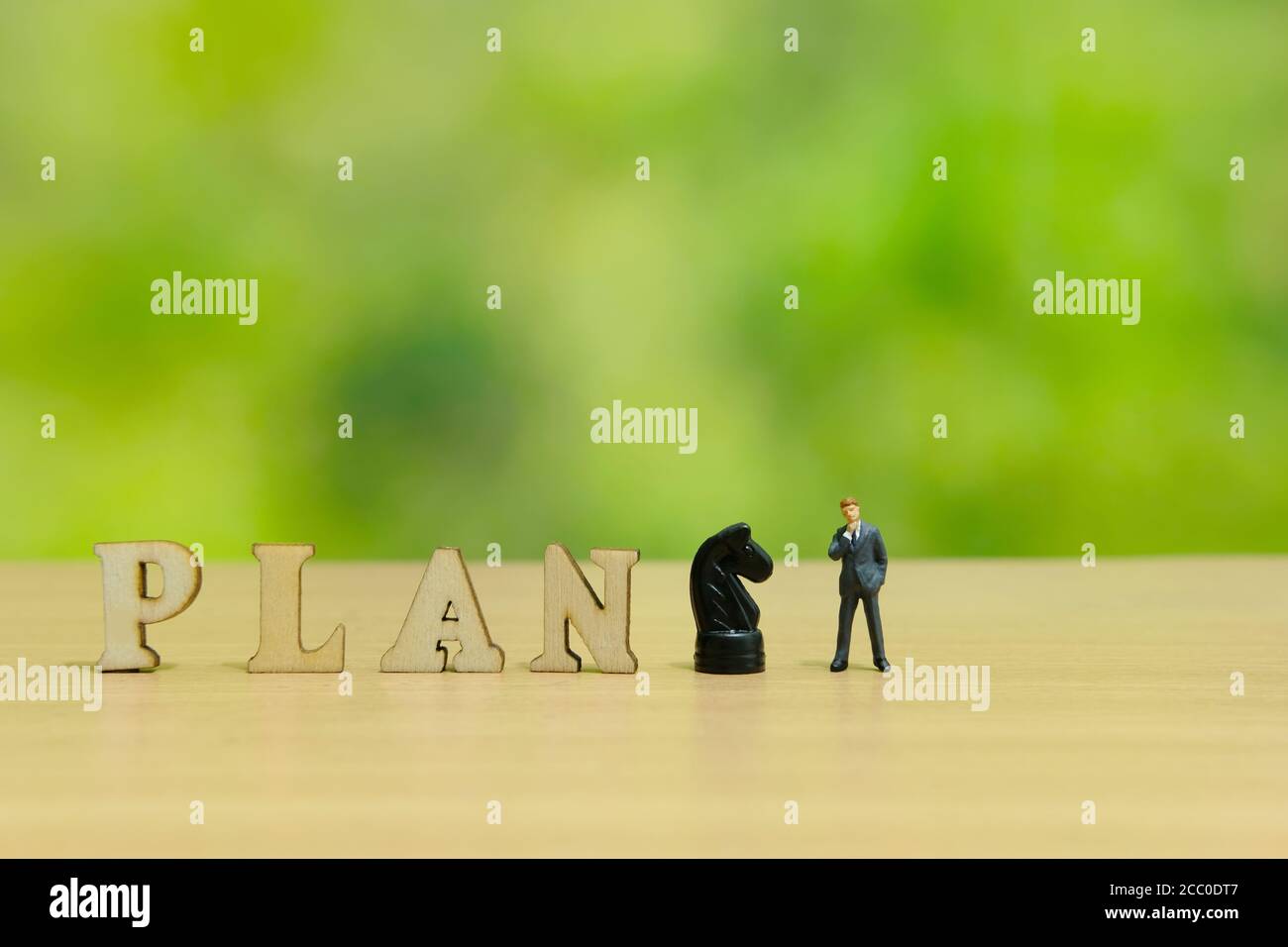 Foto concettuale strategia aziendale - miniatura dell'uomo d'affari in piedi un tavolo con la parola in pianta di legno e cavaliere Foto Stock