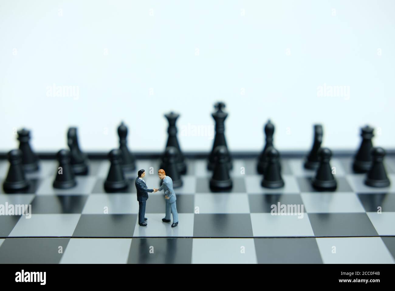 Concetto di affari in miniatura - due uomini d'affari fanno accordo di stretta di mano dentro fronte della pedina degli scacchi Foto Stock