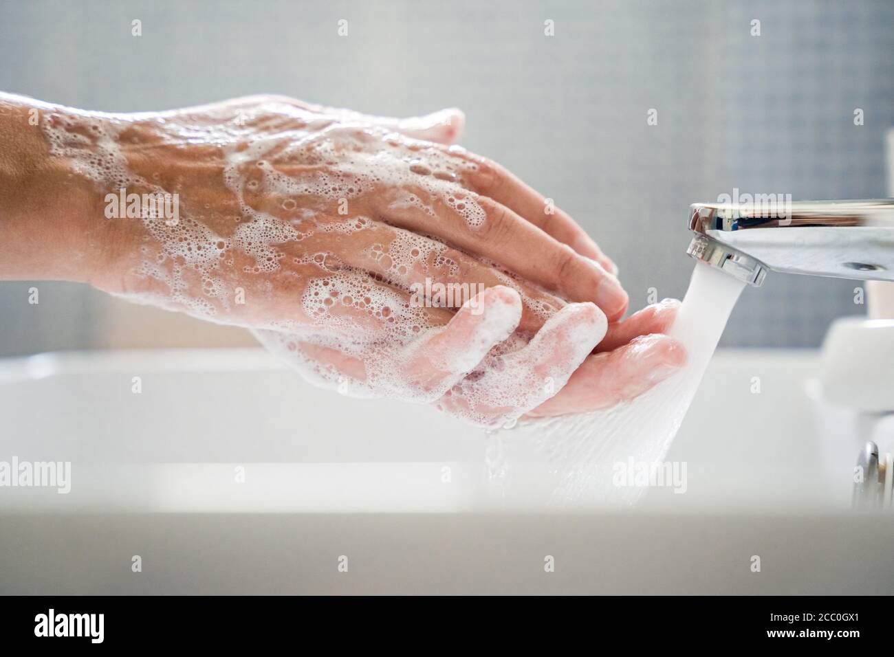 La giovane donna lava le mani nel lavabo del bagno sotto l'acqua corrente. Strofina le mani insieme al sapone. Primo piano della vista laterale Foto Stock