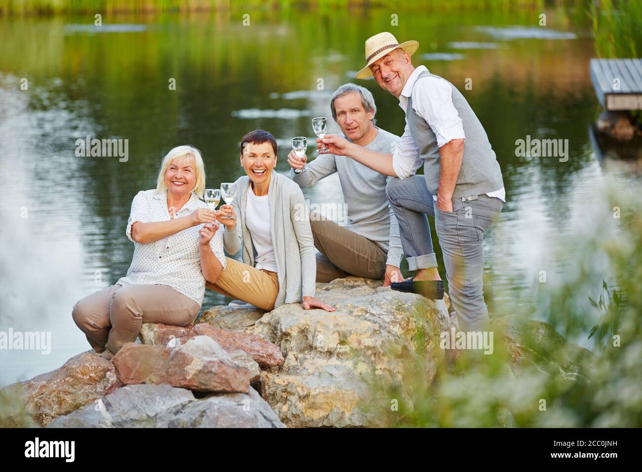 Gruppo di anziani felici seduti vicino al lago in estate con un bicchiere d'acqua Foto Stock