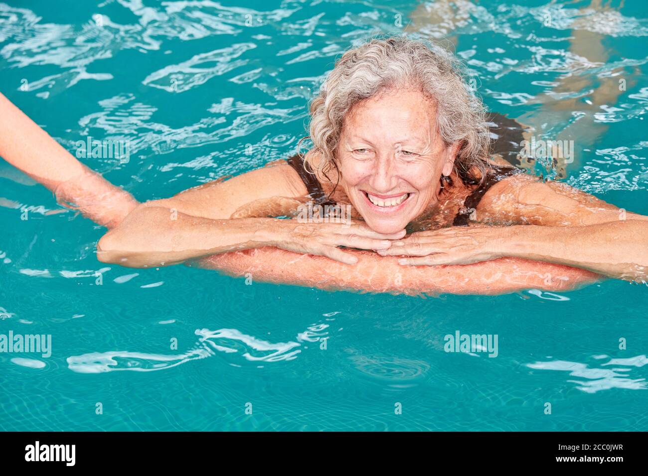 Donna anziana sorridente in piscina all'aqua fitness con un noodle per il nuoto Foto Stock