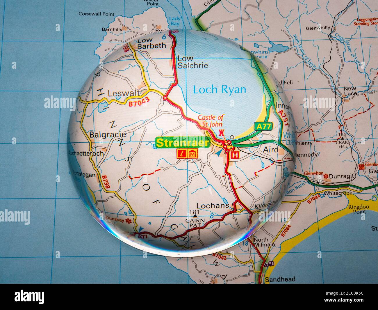 Primo piano di una lente d'ingrandimento a forma di cupola su una pagina di una mappa dell'atlante stradale britannico, con l'area di Stranraer della Scozia ingrandita per una vista più ravvicinata. Foto Stock