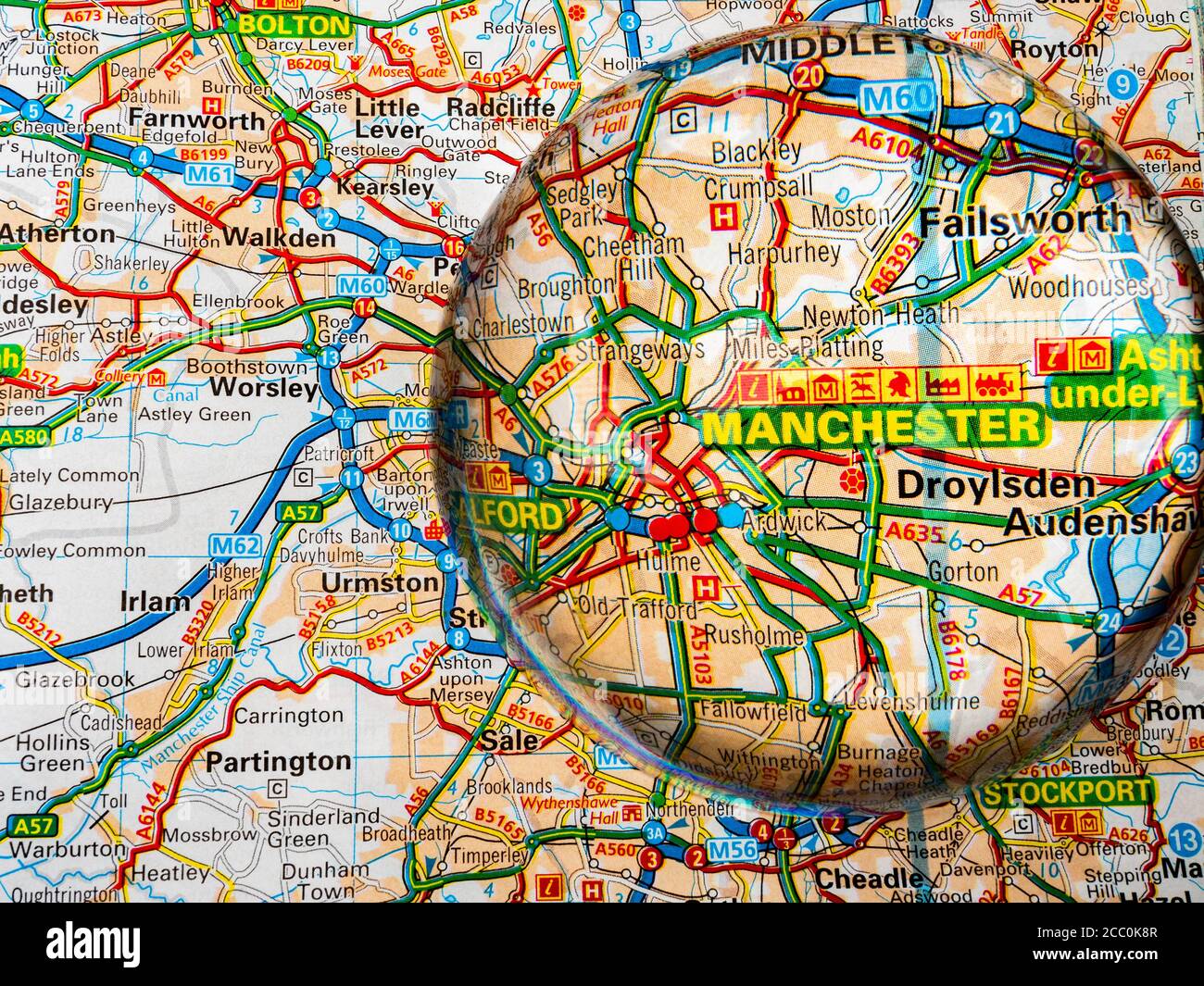 Primo piano di una lente d'ingrandimento a forma di cupola su una pagina di una mappa dell'atlante stradale britannico, con l'area di Manchester dell'Inghilterra ingrandita per una vista più ravvicinata. Foto Stock