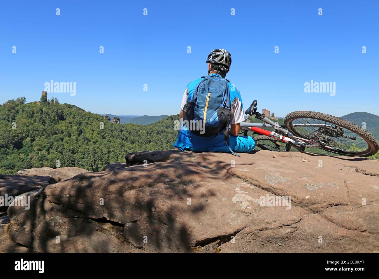 Immagine simbolo: Motociclista di montagna seduto su una roccia nella foresta di Palatinato con una vista del Castello di Trifels, Annweiler (modello rilasciato) Foto Stock