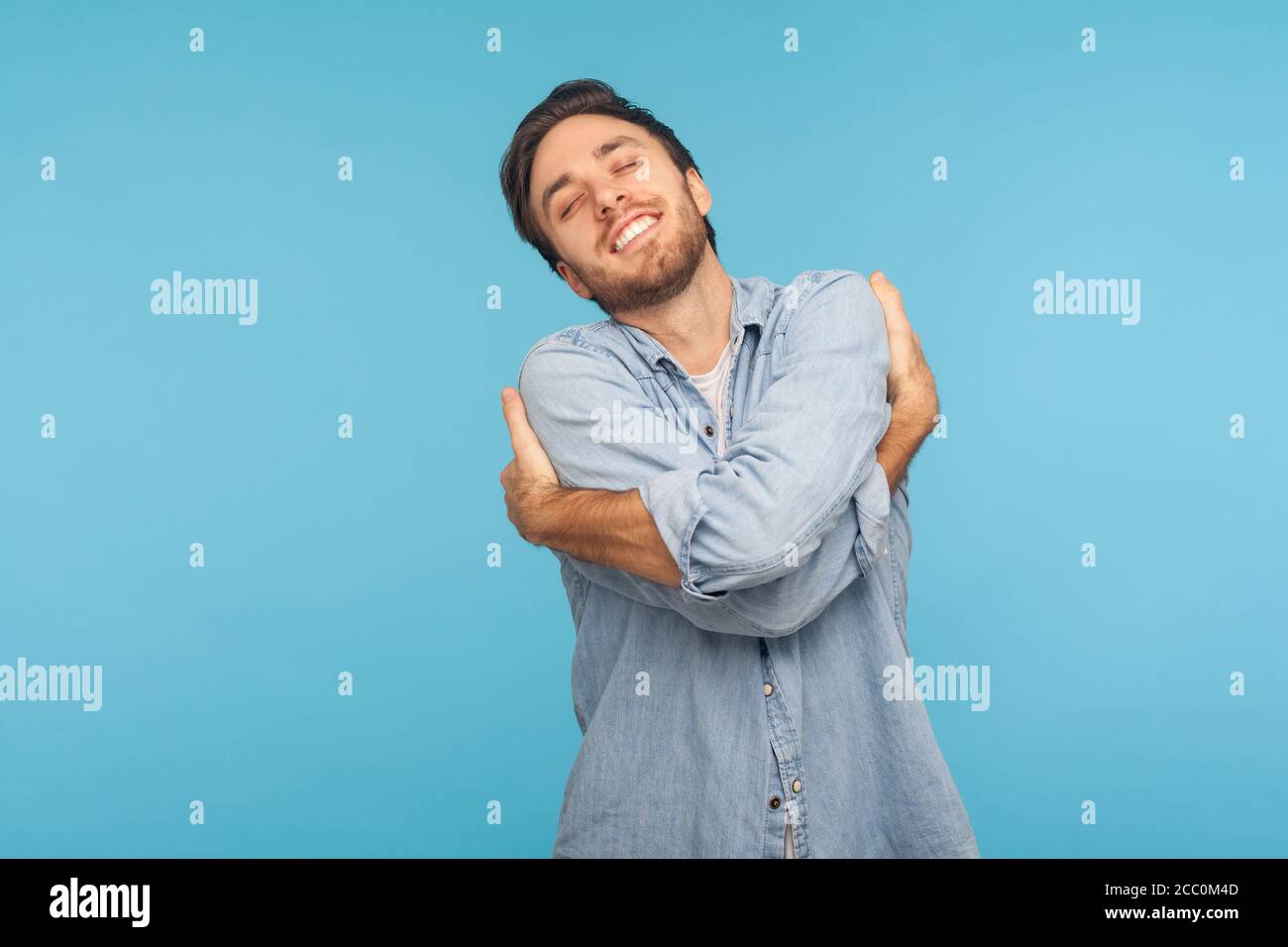 Mi voglio bene! Ritratto di uomo narcisistico egoista in camicia di denim operaio abbracciandosi e sorridendo con espressione di grande ego, piacere e sel Foto Stock