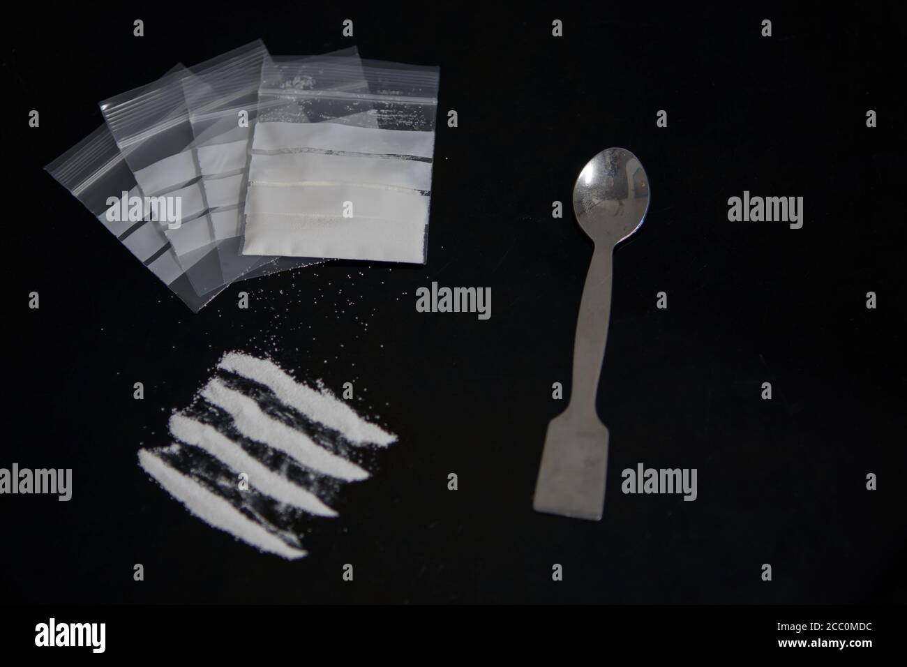Polvere di cocaina e farmaci in sacchetti di plastica su superficie di vetro nera. Vista dall'alto del concetto di tossicodipendenza Foto Stock