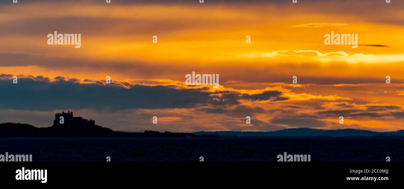 Il castello di Bambburgh, Northumberland, si stagliava contro un suggestivo cielo arancione al tramonto, preso da una barca in mare. Foto Stock