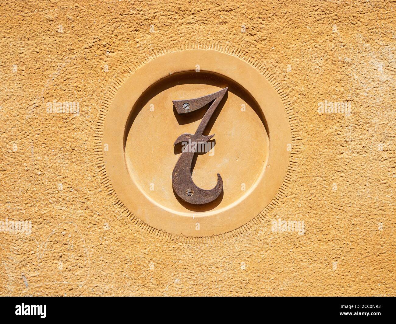 Porta in metallo arrugginito segno numero 7 sulla parete arancione in una giornata di sole Foto Stock