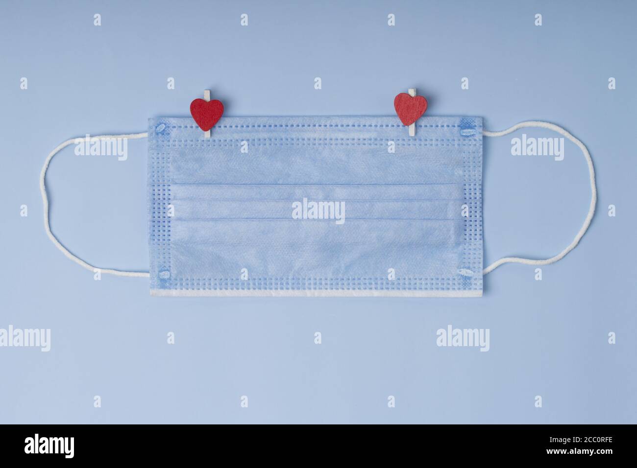 Concetto di amore nella nuova realtà normale. Maschera medica di protezione con i vestiti di legno con i cuori su sfondo blu. Foto Stock
