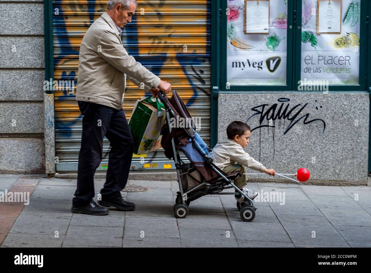 MADRID, SPAGNA - 28 aprile 2015: Madrid / Spagna - 27 2015 aprile: Vecchio uomo con una borsa di plastica e una carrozza con un bambino che ha una mongolfiera rossa Foto Stock