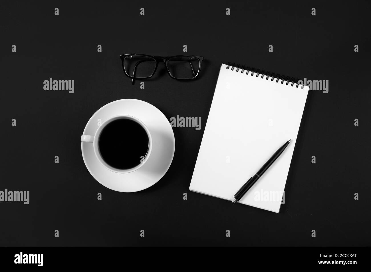tazza da caffè e blocco note bianco con penna su sfondo nero. vista dall'alto Foto Stock