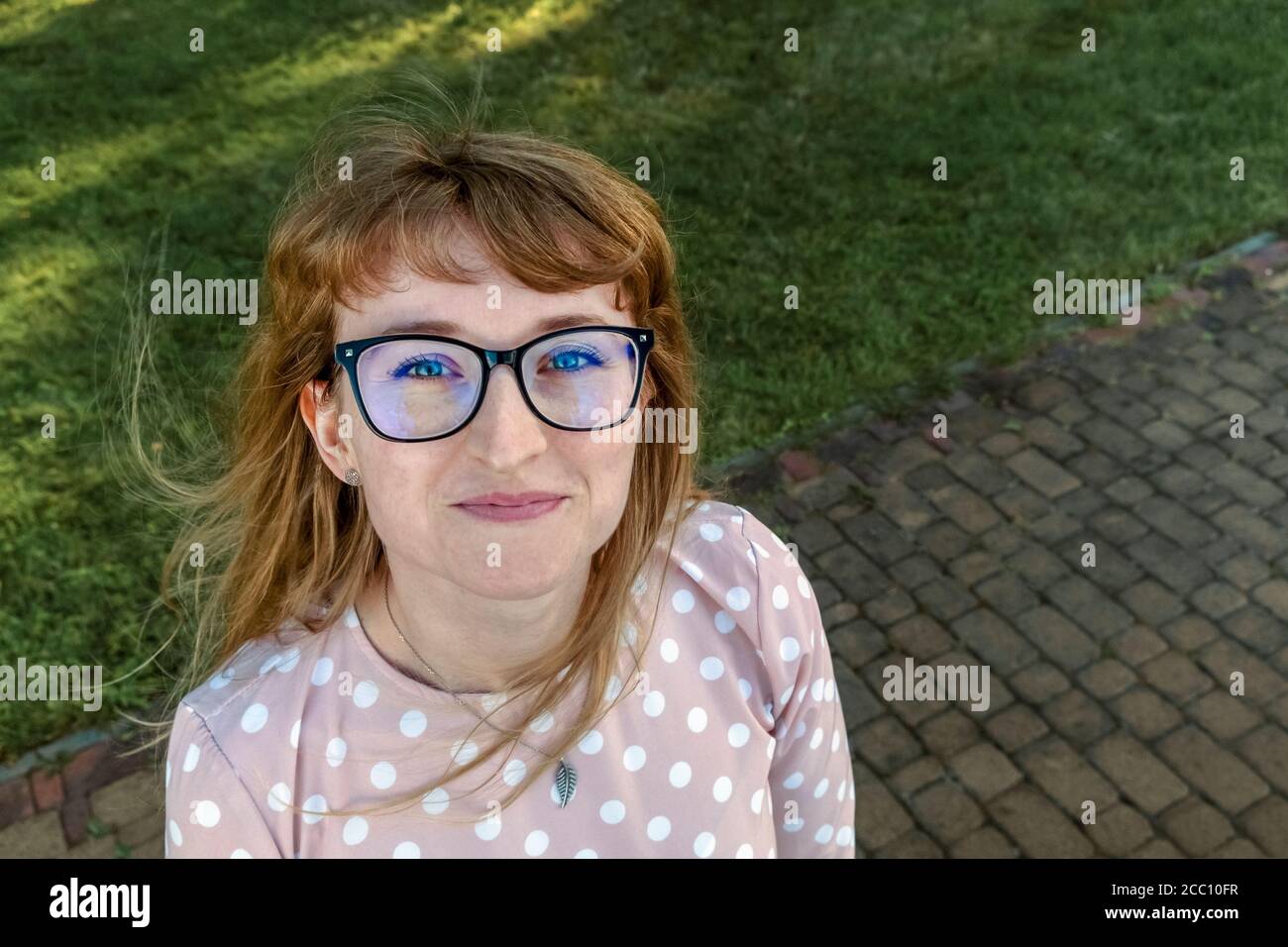 Ragazza rossa felice con gli occhiali che guardano la macchina fotografica dal basso verso l'alto Foto Stock