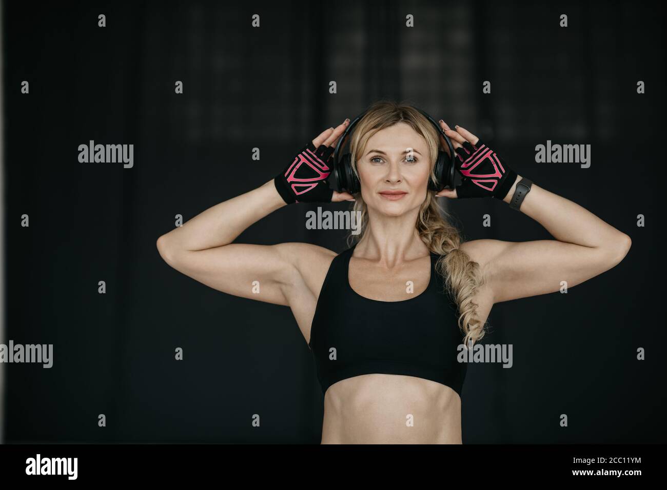 Musik, stile sportivo e stile di vita sano in mezza età. Donna amichevole con fitness tracker, guanti e cuffie Foto Stock