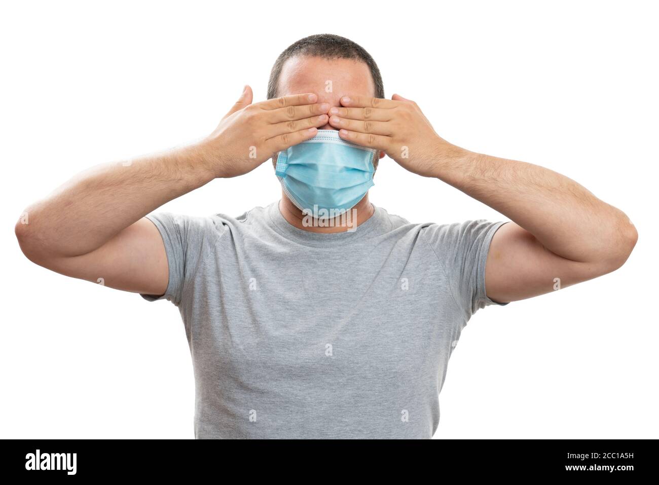 Modello maschio bianco che indossa una maschera monouso per la prevenzione della malattia influenzale coprendo gli occhi con le palme come concetto segreto di sorpresa durante la pandemia isol Foto Stock