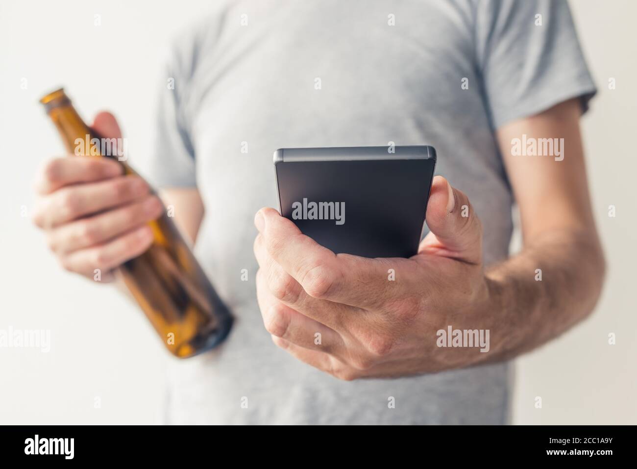 Bere birra e utilizzare lo smartphone, primo piano delle mani maschili con messa a fuoco selettiva Foto Stock
