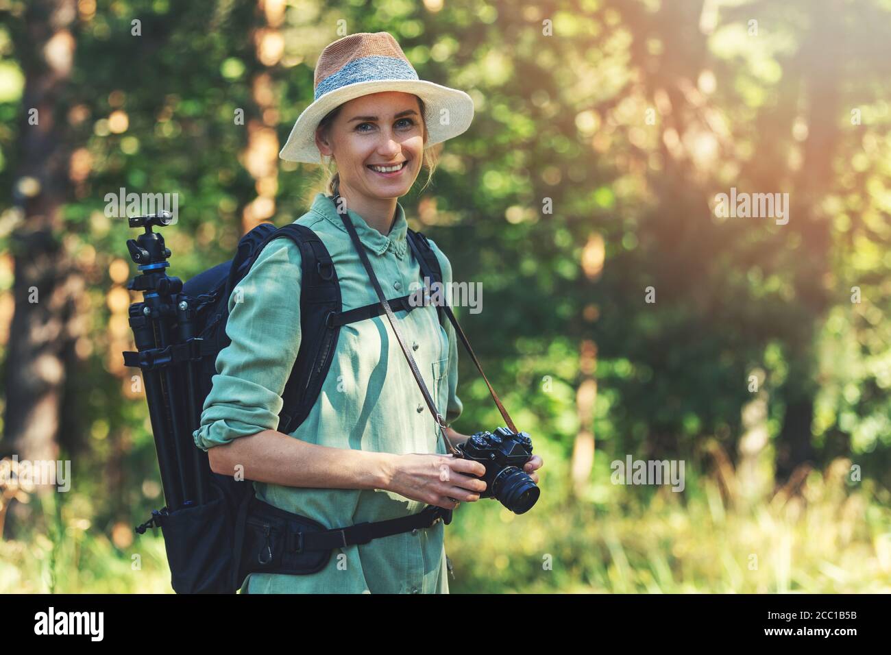 sorridente fotografa di natura femminile con una videocamera analogica in foresta Foto Stock