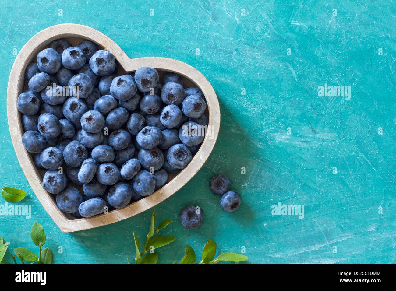 Mirtilli freschi maturi in ciotola a forma di cuore su sfondo blu con spazio per la copia del testo Foto Stock