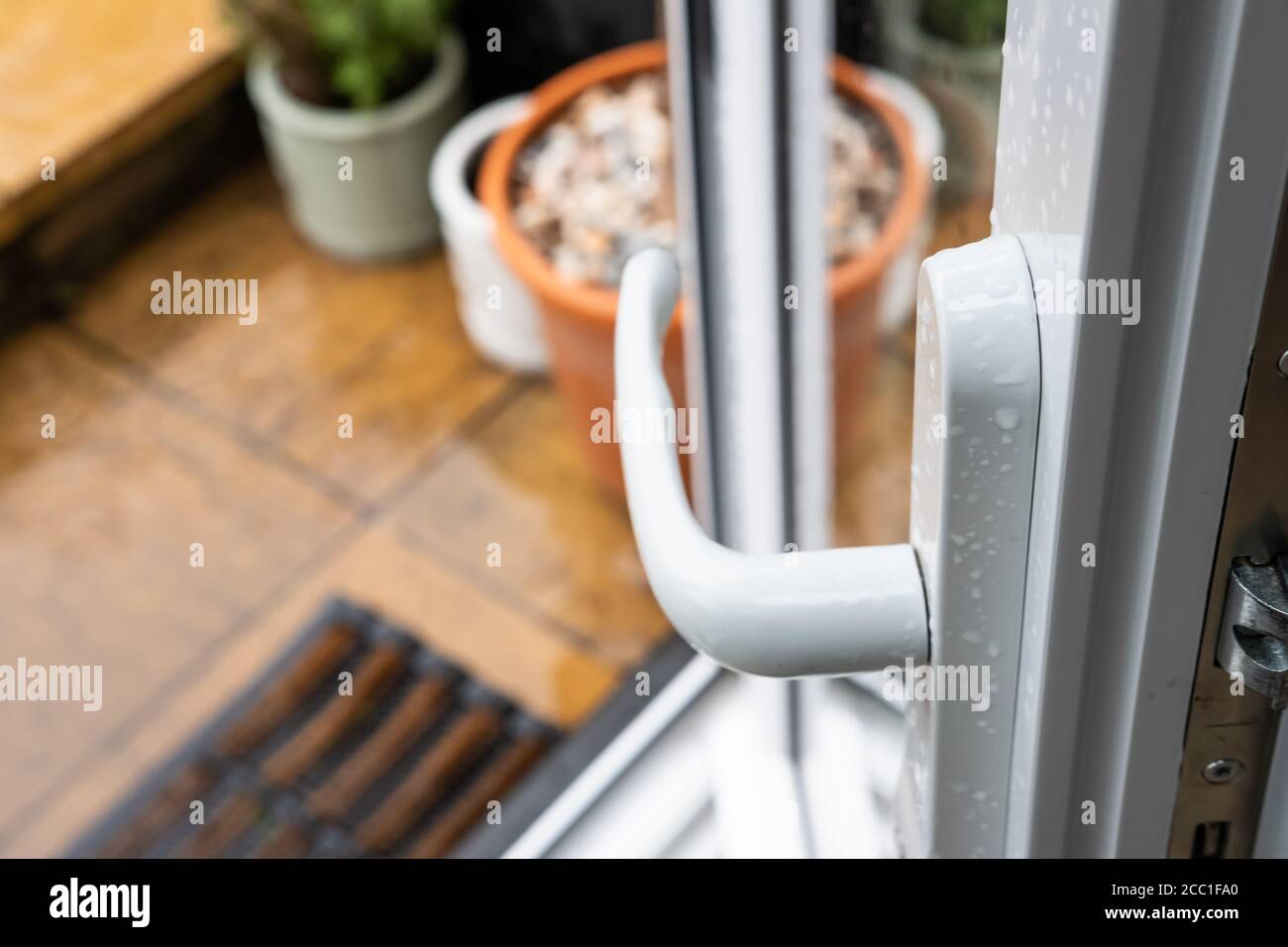 Messa a fuoco superficiale di una porta da patio uPVC appena installata, visto aperto che conduce ad un'area da patio umida sul retro di una casa. Foto Stock