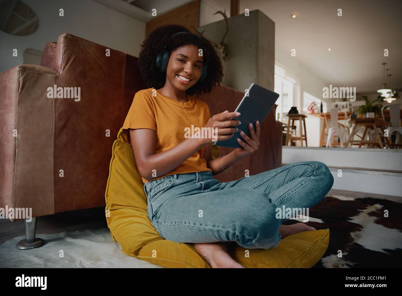 Vista ritratto ad angolo basso di una bella giovane donna che guarda il video a casa utilizzando un tablet digitale con cuffie wireless Foto Stock