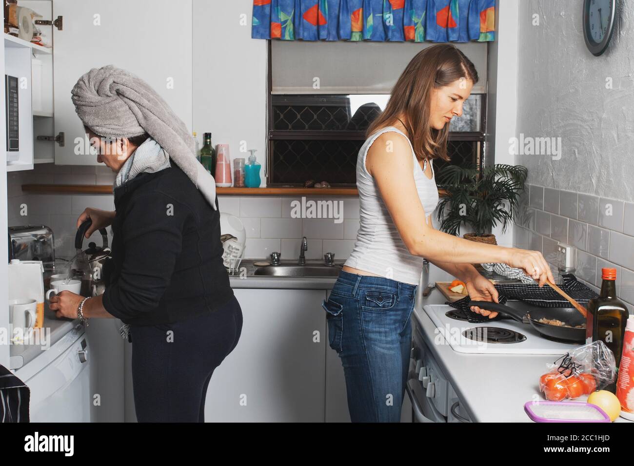 Due donne di mezza età stanno cucinando la cena, parlando e ridendo in una cucina Foto Stock