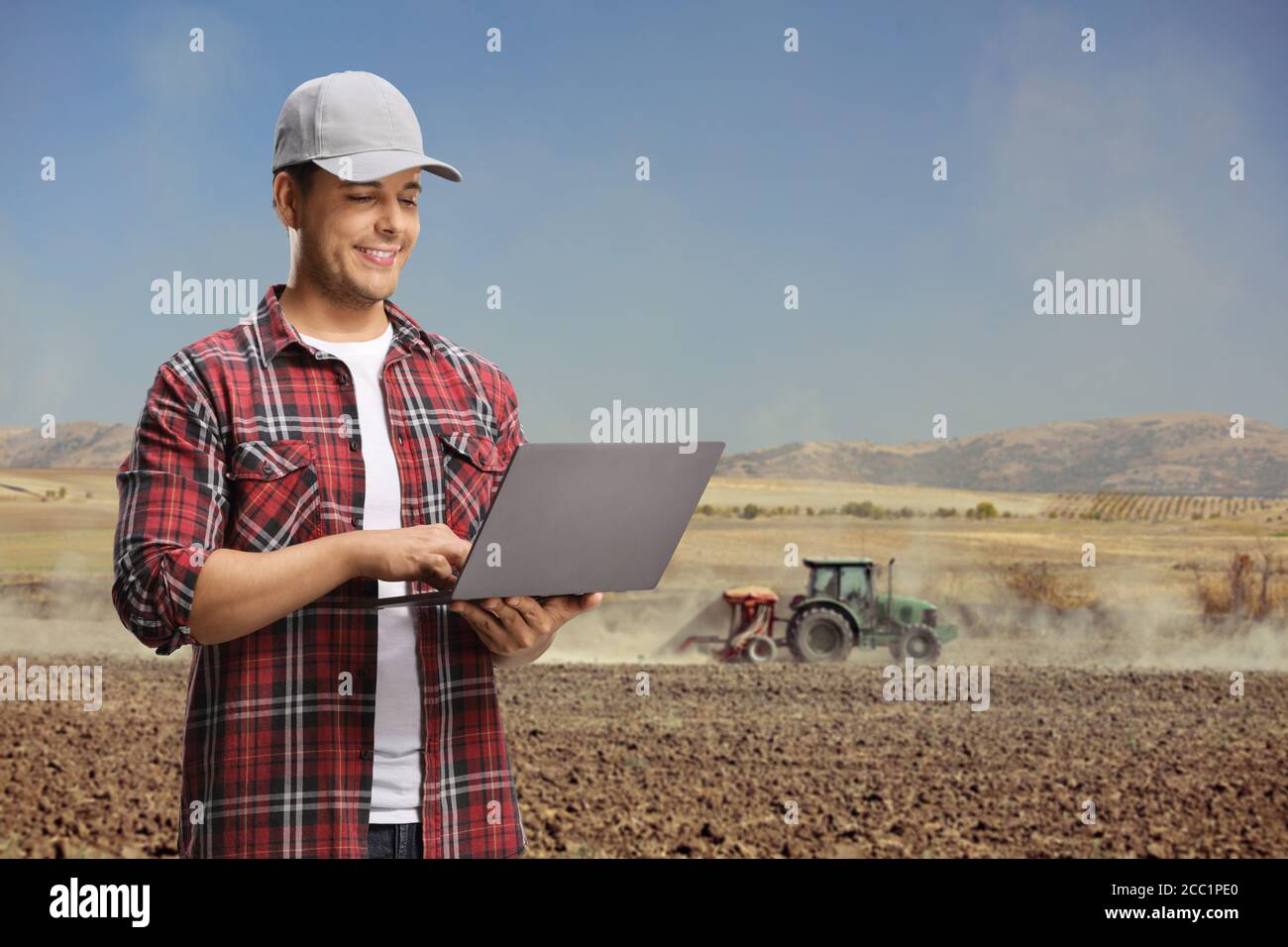 Giovane ingegnere agricolo che usa un computer portatile su un campo con un trattore Foto Stock