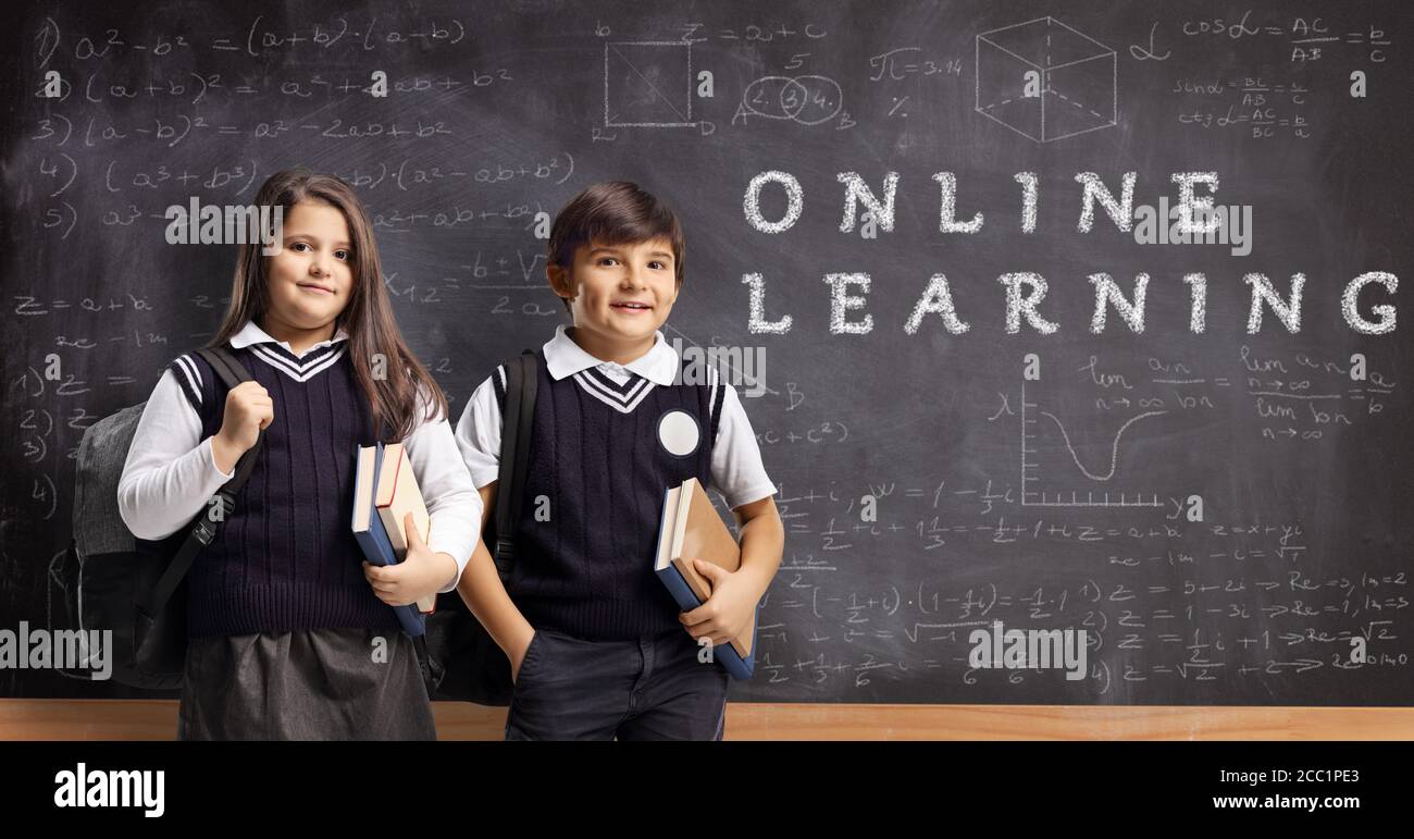 Scolari in uniforme con libri e zaini davanti una lavagna con apprendimento online di testo Foto Stock